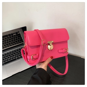 Close-up of deep pink crossbody bag with golden round lock and buckled straps detail