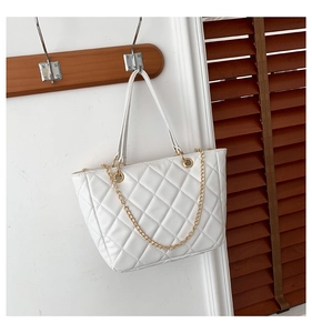 Détail d'un sac cabas matelassé blanc avec chaîne dorée sur un cintre en bois