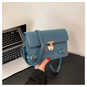 Detail view of grey-blue leather handbag with gold metal lock and adjustable shoulder strap