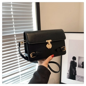 Detail of black faux leather shoulder bag with gold circular metal lock and decorative straps