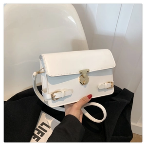 Detail of white rectangular crossbody bag with golden round lock and twin belt buckles