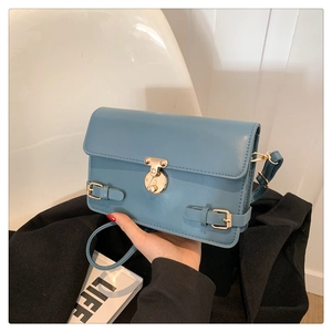 Close-up of blue faux leather shoulder bag with a gold round lock and buckle details