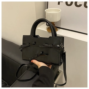 Vue détaillée d'un sac à main noir en cuir verni avec des nœuds décoratifs élégants