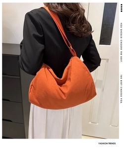 Large orange nylon hobo crossbody bag styled with a black blazer and white skirt