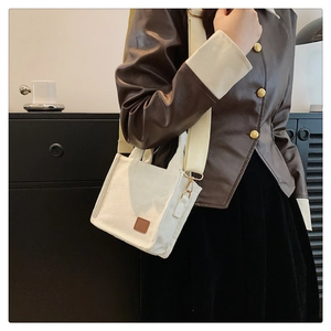 Detail einer weißen Cord-Umhängetasche mit braunem Lederpatch und breitem Gurtband