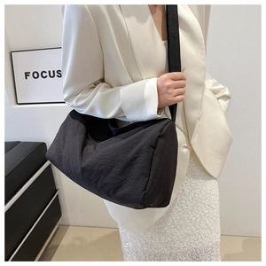 Minimalist black large capacity crossbody bag styled with white blazer in indoor setting