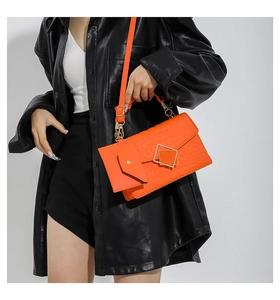 Detail of bright orange crocodile embossed crossbody bag with gold metal buckle