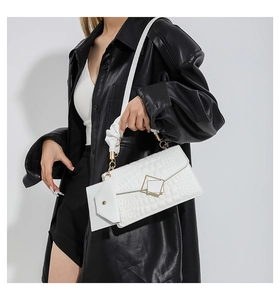 Macro view of white crocodile pattern shoulder bag with golden geometric clasp detail