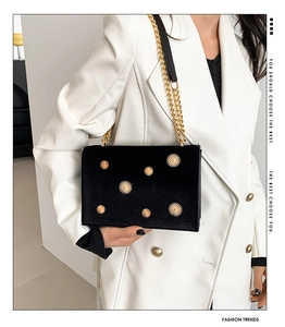 Detalle de bolso bandolera de terciopelo negro con sol dorado y cadena metálica