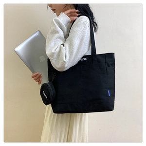 Detalle de un bolso tote grande de lona negra con etiqueta de moda y pequeño monedero