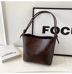 Détail d'un sac seau en cuir marron foncé avec bandoulière à nœud et finitions dorées