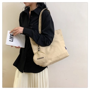 Detalle de bolso tote de lona beige con bolsillo frontal y colgante redondo de moda