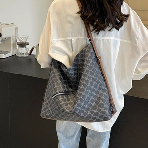 Grey geometric print crossbody tote bag with brown leather strap in a cafe setting