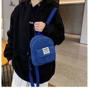 Close-up of blue corduroy mini backpack featuring decorative white patch and striped texture