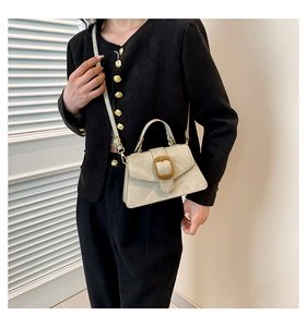 Detalle de bolso beige con hebilla dorada ovalada y correa de hombro ajustable