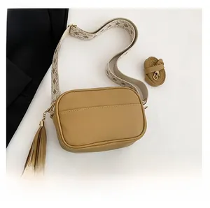 Detail of khaki crossbody bag with textured leather, tassel charm, and two straps