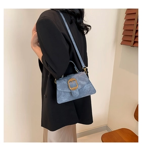 Détail d'un sac à bandoulière vintage bleu avec boucle dorée sur un mannequin en blazer noir