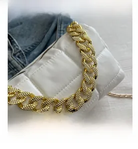 Close-up of white quilted handbag featuring a textured chunky gold chain and metal strap