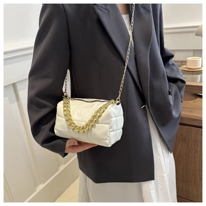 Detail of a quilted crossbody bag with chunky gold metal chains and textured off-white leather
