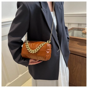 Detail of a brown quilted square shoulder bag with gold chain strap on a model