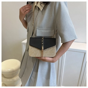 Détail du sac bandoulière en paille avec pompon en chaîne dorée et rabat en cuir noir