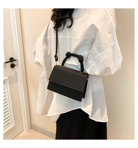 Detail of black woven crossbody bag with knot handle and gold hardware on model