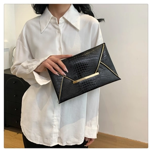 Close-up of black crocodile texture envelope clutch bag with elegant gold metal trim