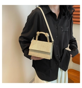 Detail of woven straw crossbody bag featuring cylindrical top handle and flap closure