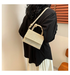 Close-up of beige woven crossbody bag with knot handle worn by model in soft light