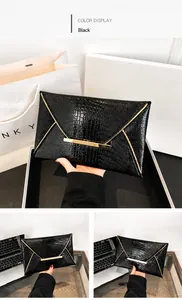 Detail of black faux leather envelope clutch featuring crocodile pattern and gold metal trim