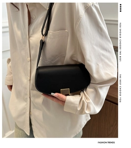 Side view of black leather saddle bag with gold striped buckle worn by a model