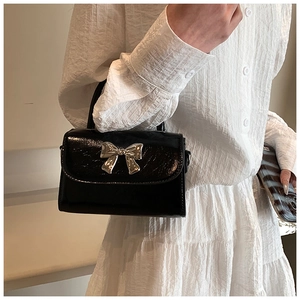 Détail du sac à main en cuir verni noir avec nœud en métal argenté brillant