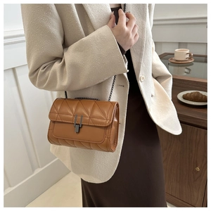 Détail du sac matelassé marron avec chaîne et fermoir en métal sur fond de blazer beige