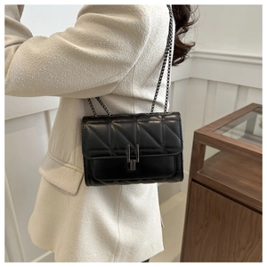 Détail d'un sac bandoulière en cuir noir matelassé avec chaîne métallique et fermoir en U