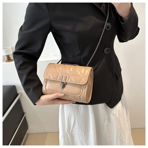Détail du sac bandoulière beige matelassé avec fermoir noir porté sur une veste noire