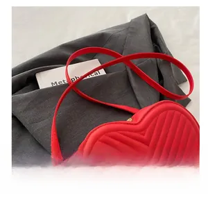 Détail du sac à main rouge en forme de cœur avec matelassage en V sur blazer gris