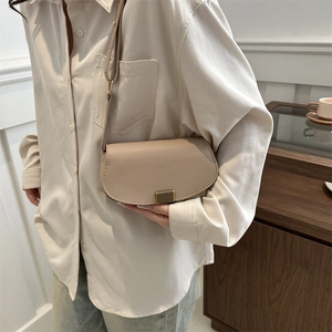 Elegant beige saddle bag with vintage metal clasp worn as a crossbody on a model