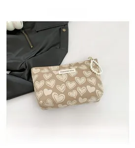 Detail of heart-patterned canvas toiletry bag with elegant pearl strap and logo tag