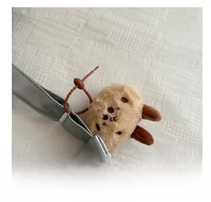 Gros plan d'un charm en peluche kaki avec broderie sur la bandoulière d'un sac argenté