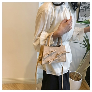 Detail of beige bow-knot handbag featuring matte texture and cylindrical double handles