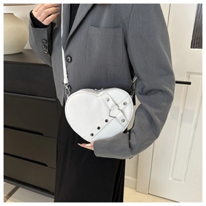 Detail van witte hartvormige crossbodytas met zilveren gespen en metalen klinknagels