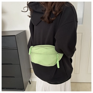 Sac banane en toile vert clair porté par un mannequin avec un sweat à capuche noir