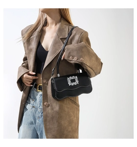 Sac à bandoulière noir avec fond ondulé et boucle en strass porté par un mannequin