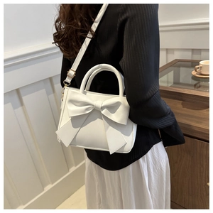 Dettaglio di una borsa bianca con fiocco e tracolla dorata indossata da una modella