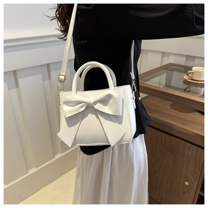 Detail of white PU leather crossbody bag featuring a large decorative bow and top handle