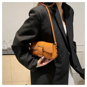 Close-up of orange-brown leather baguette bag with gold buckle on model's shoulder
