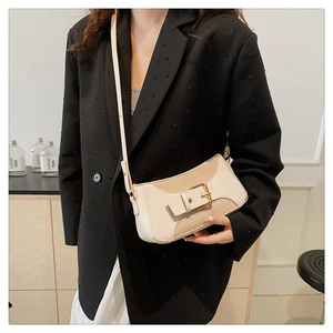 Detail of beige contrast crossbody bag with large gold buckle on model with black blazer