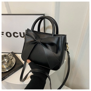 Detail of black faux leather handbag with oversized bow and gold metallic hardware