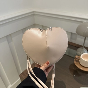 Elegant cream heart-shaped crossbody bag with gold zippers held in a cozy cafe setting