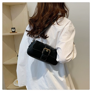 Elegant black shoulder bag with large gold buckle worn by model in a soft minimalist setting